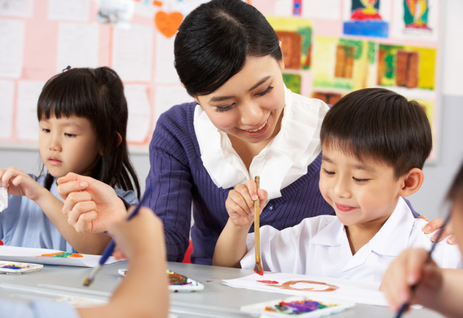 Teacher assisting young students with a classroom activity in a holiday programme
